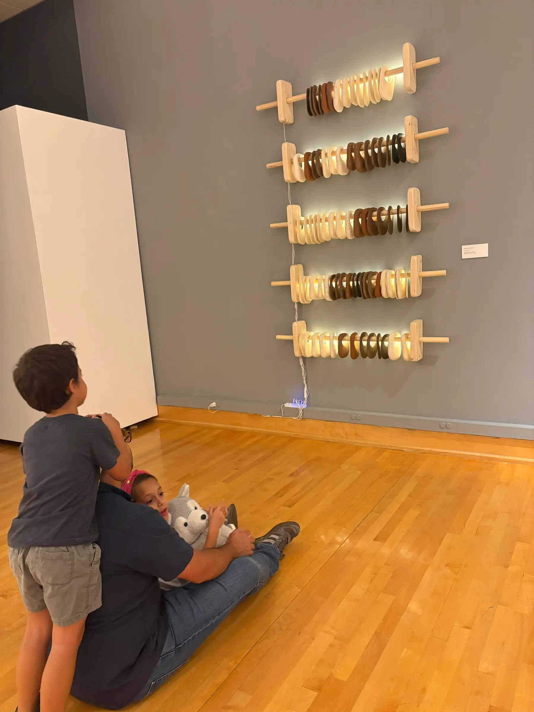 Visitors viewing the illuminated ceramic installation on the gray gallery wall