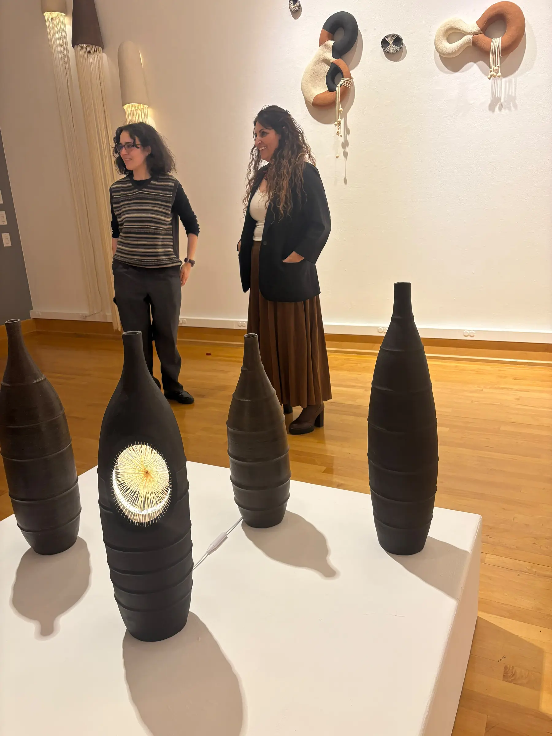 Two guests standing beside the ceramic vessels and wall sculptures