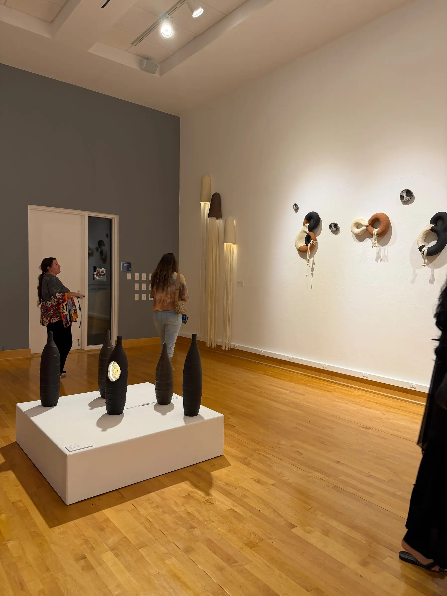 Wide exhibition view with pedestal vessels and wall-mounted sculptures