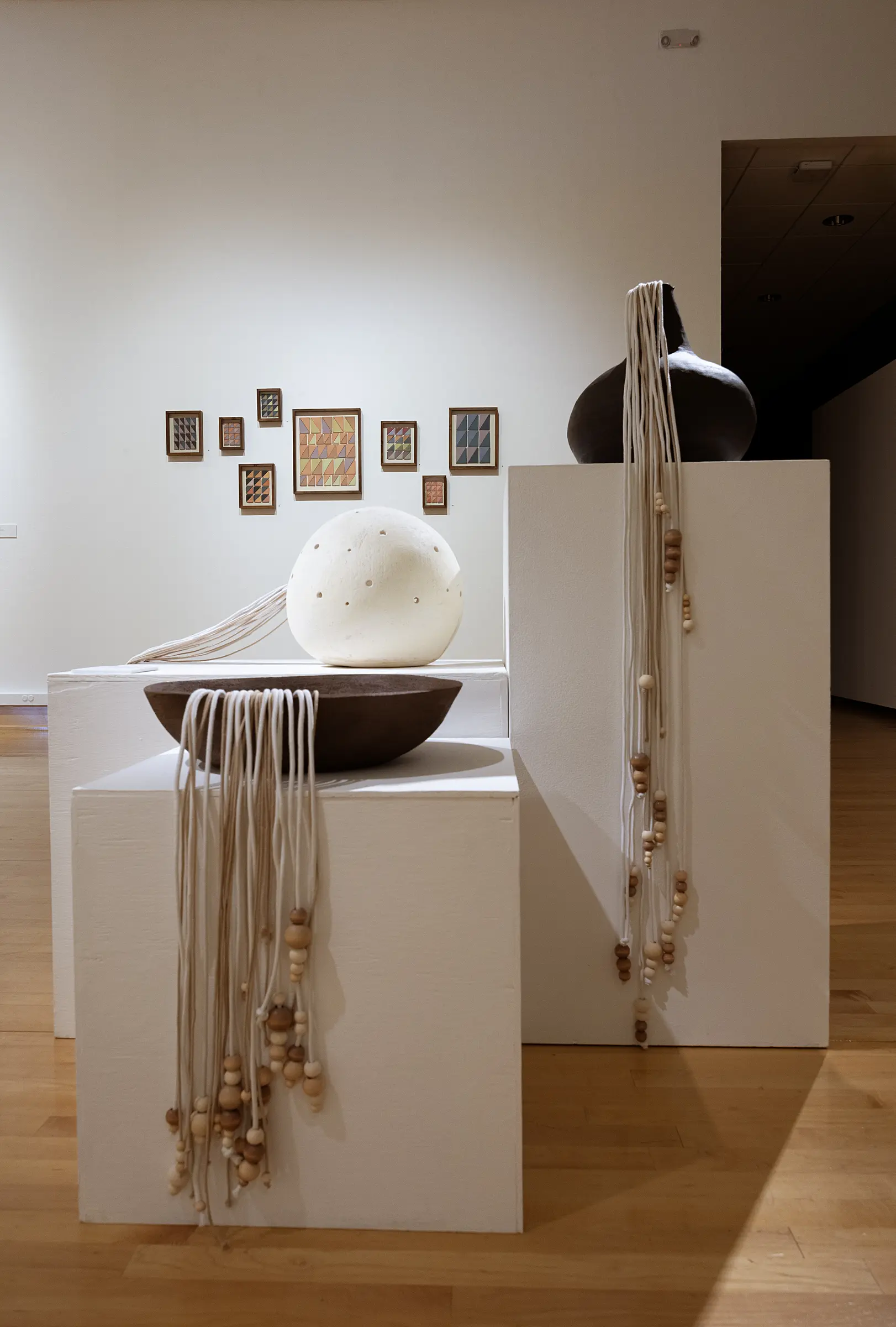 White spherical ceramic form and brown bowl displayed on adjacent pedestals