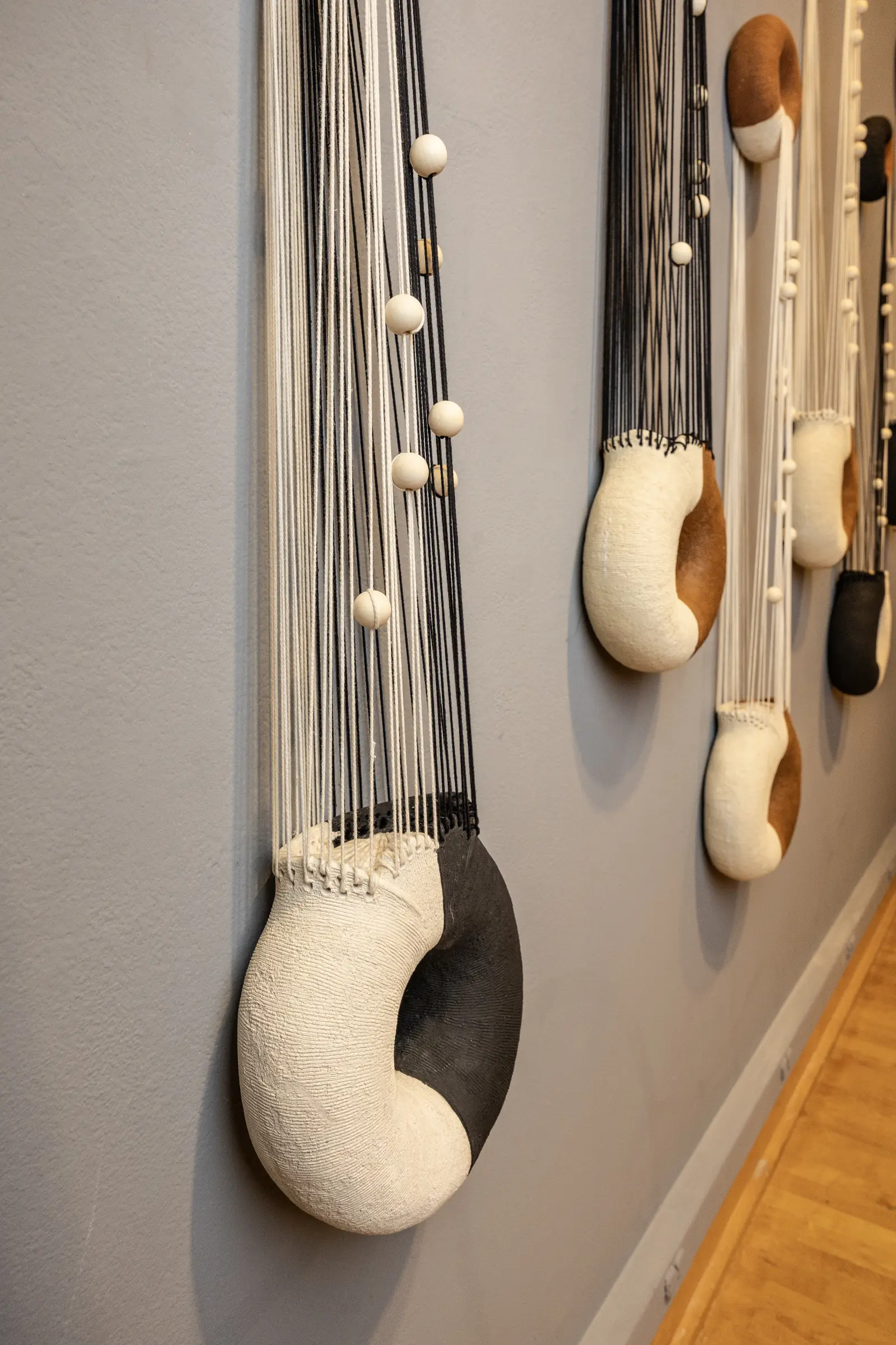 Detail of hanging black and white ceramic forms with fiber and wooden beads