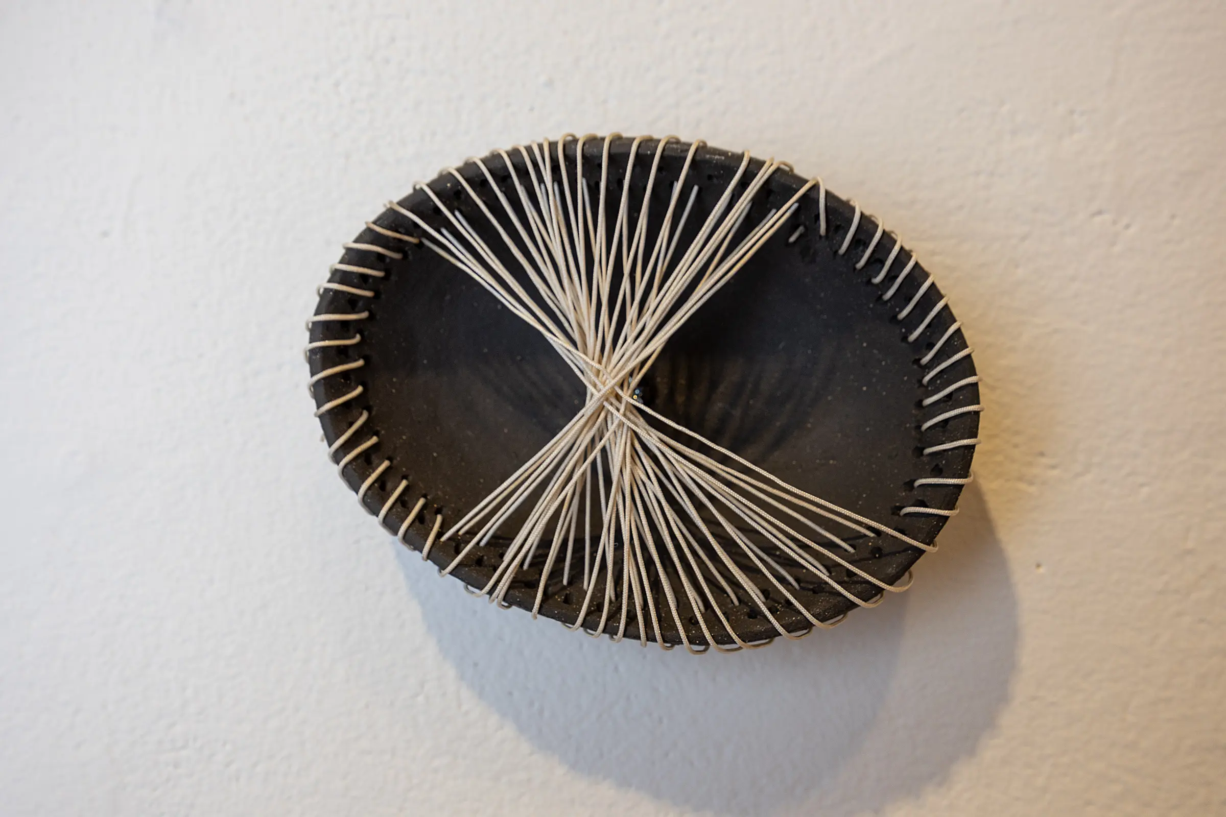 Black circular ceramic wall form wrapped with pale fiber