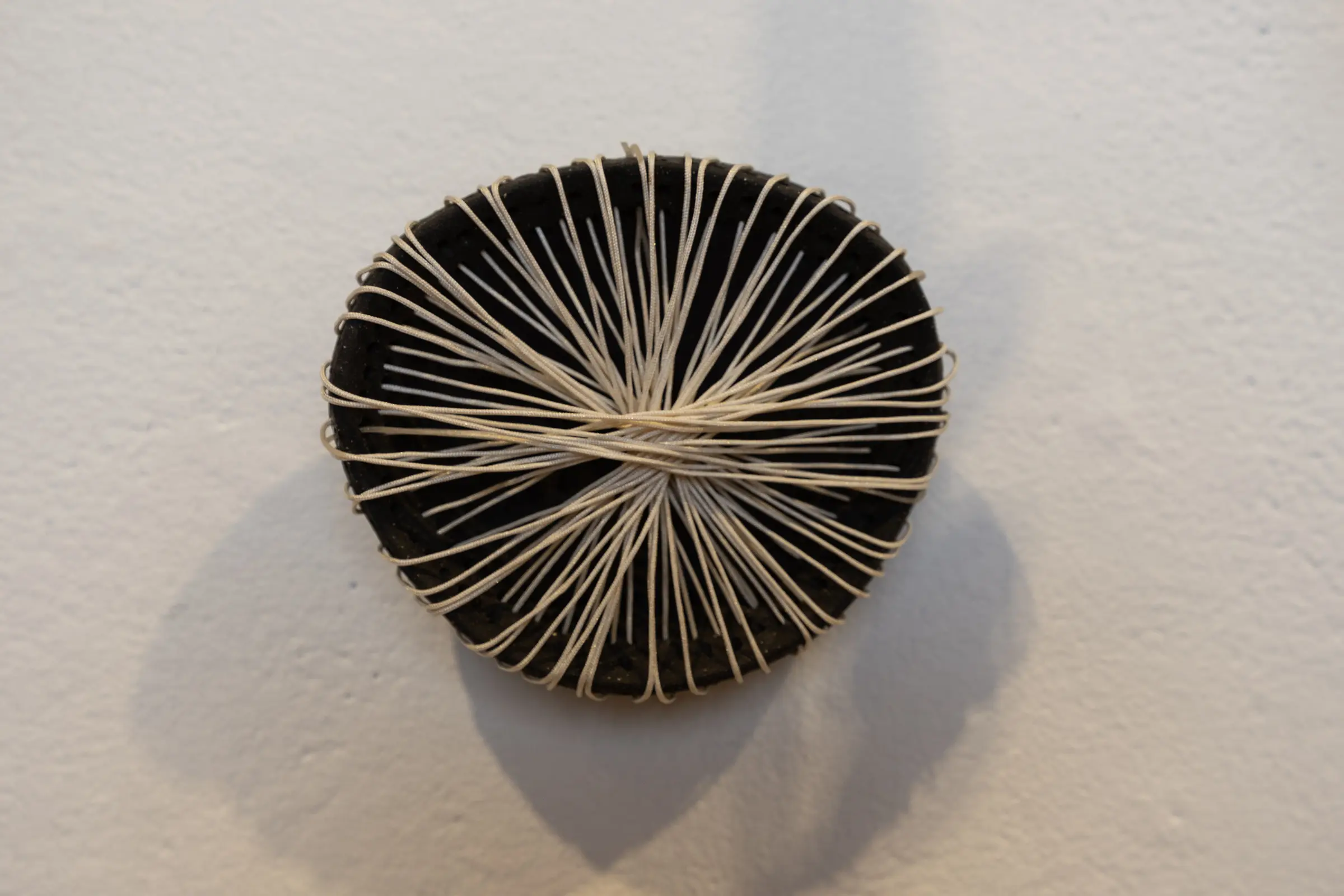 Circular black ceramic wall form with fiber crossing its center