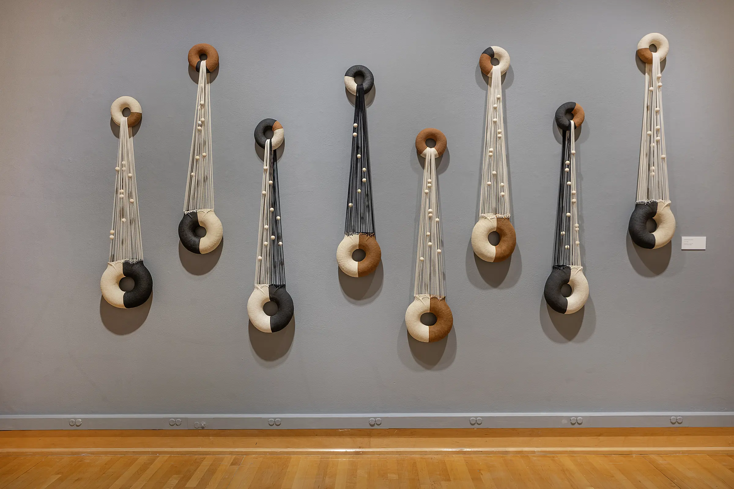 Eight ceramic and fiber sculptures suspended across the gray gallery wall