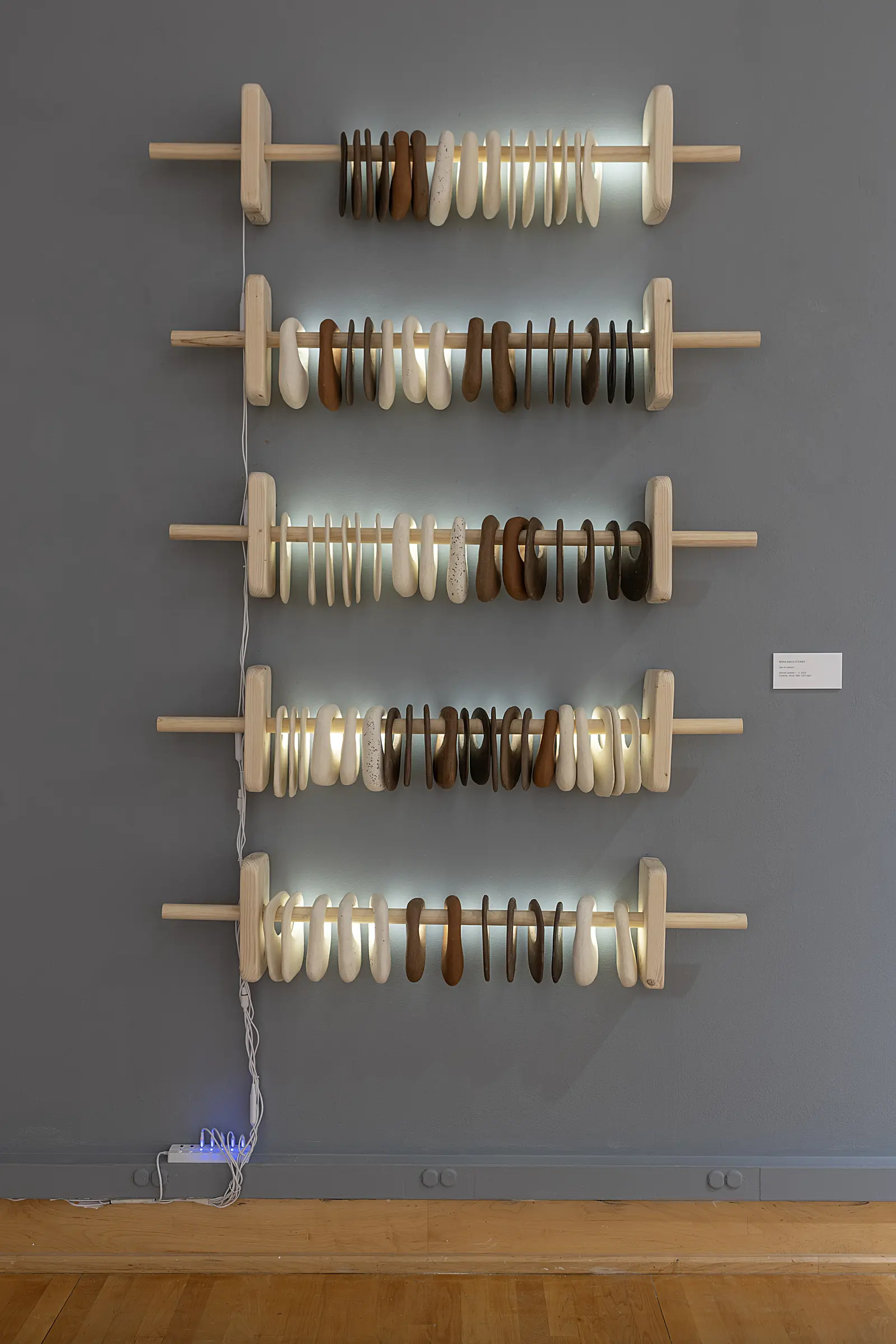 Five illuminated rows of ceramic forms arranged on wooden rods