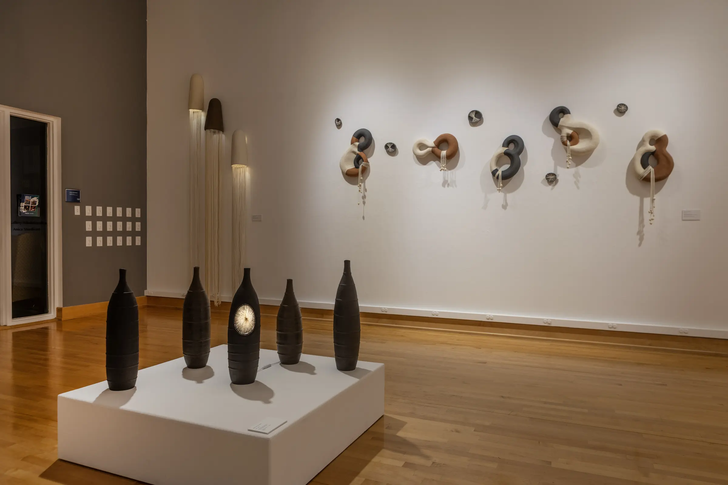 Black ceramic vessels installed in front of the looped wall sculptures