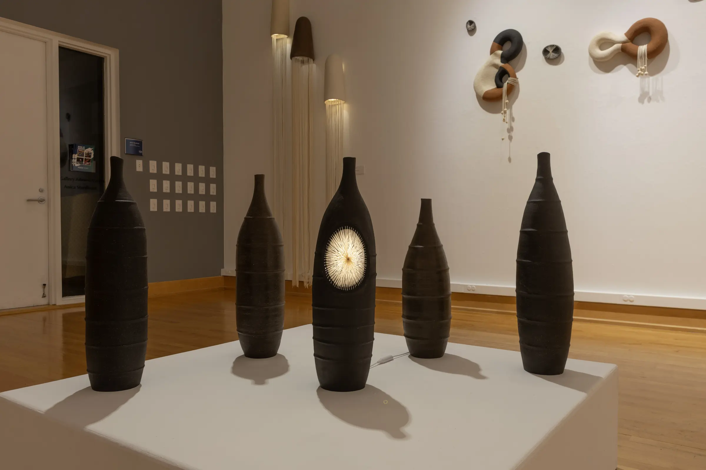 Five tall black ceramic vessels displayed together on a low pedestal