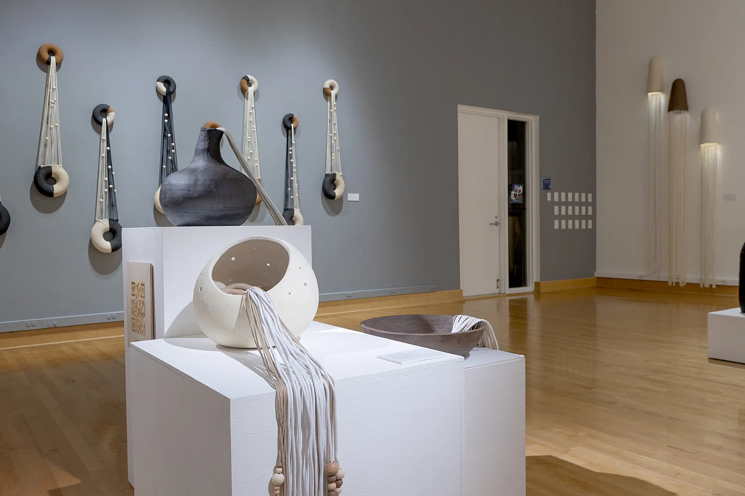 Pedestal sculptures framed by the suspended works and ceramic lamps