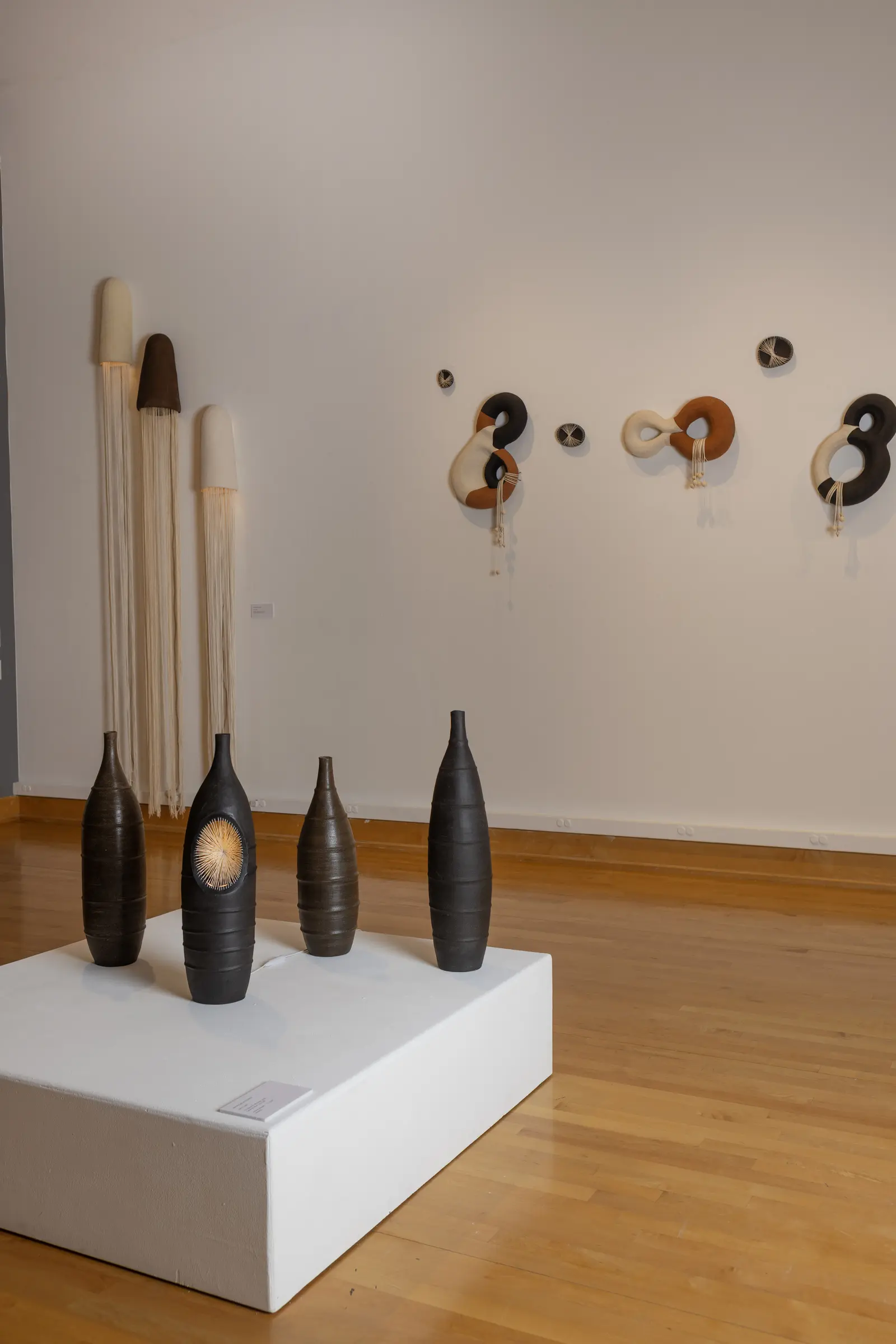 Black ceramic vessels displayed beneath the interlocking wall sculptures
