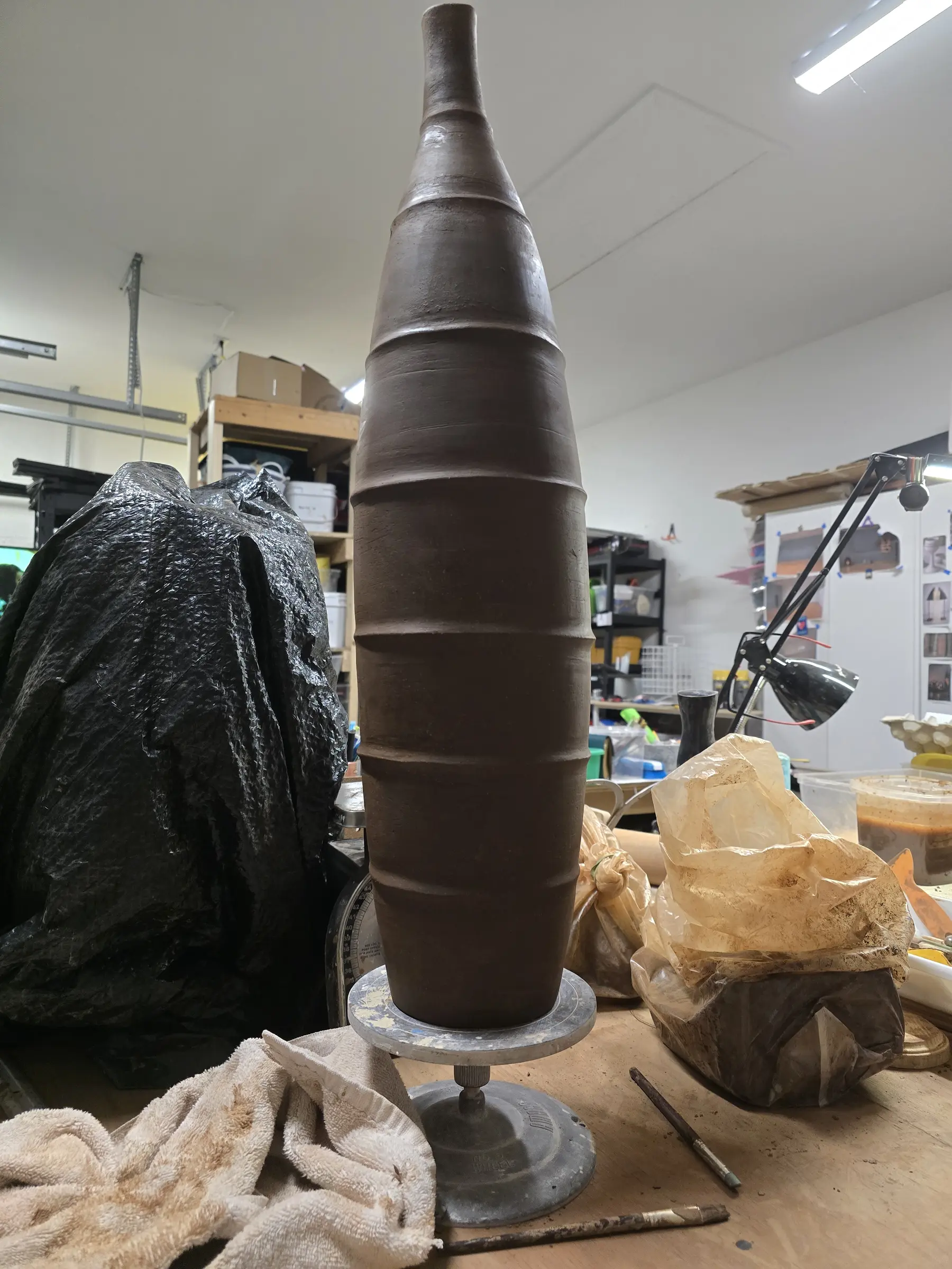 Tall coiled clay vessel rising from the pottery wheel
