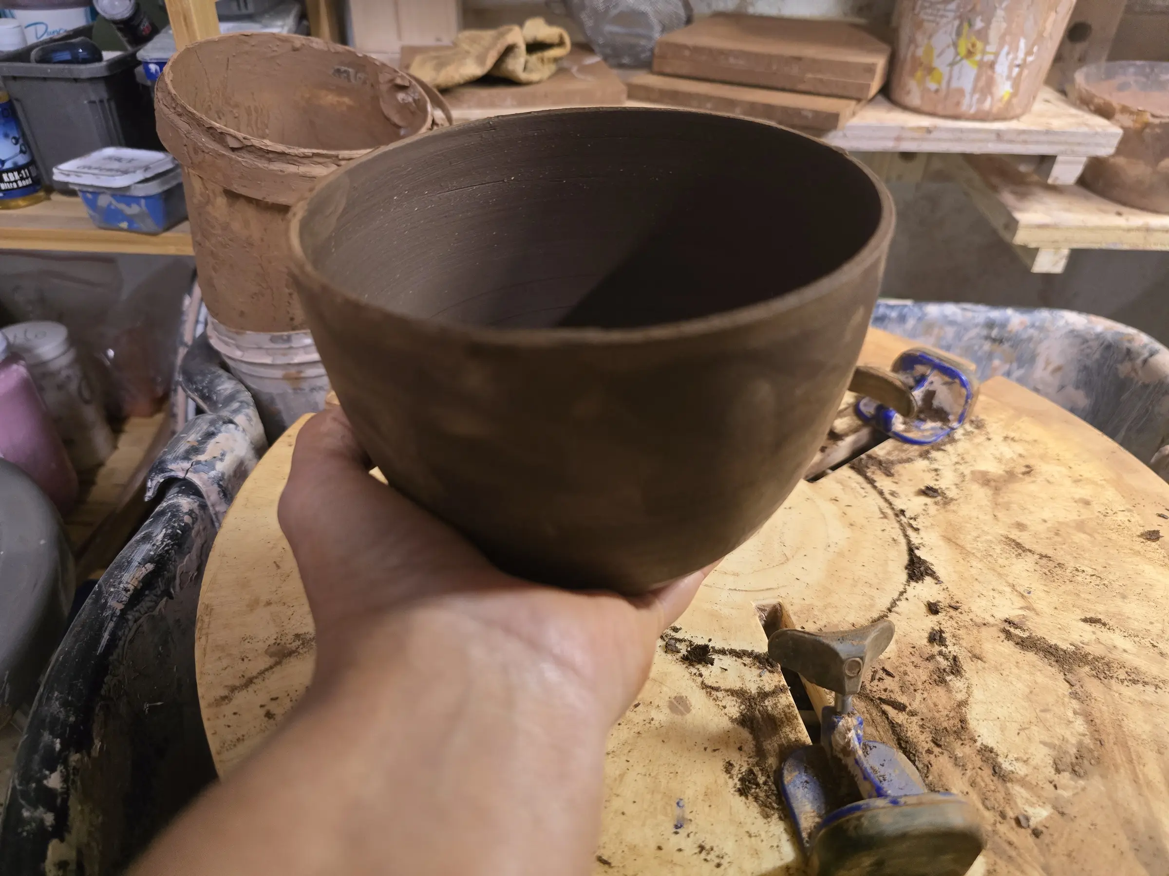 Small brown clay bowl held above the studio worktable