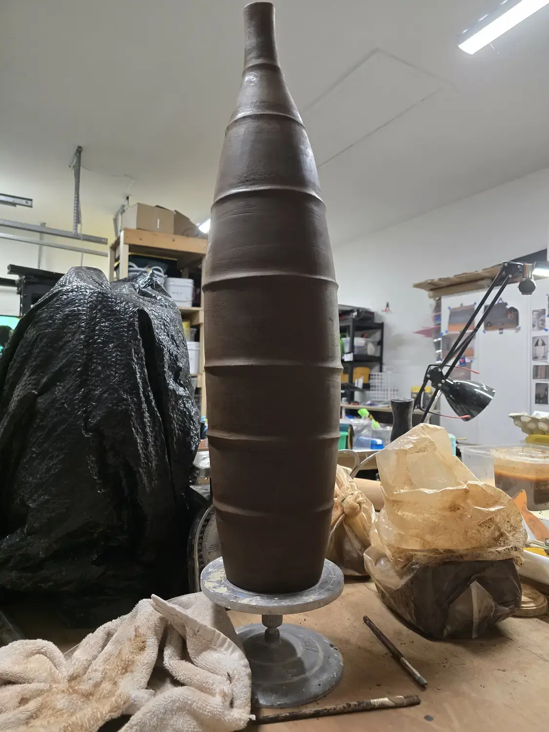 A tall segmented clay vessel on a wheel