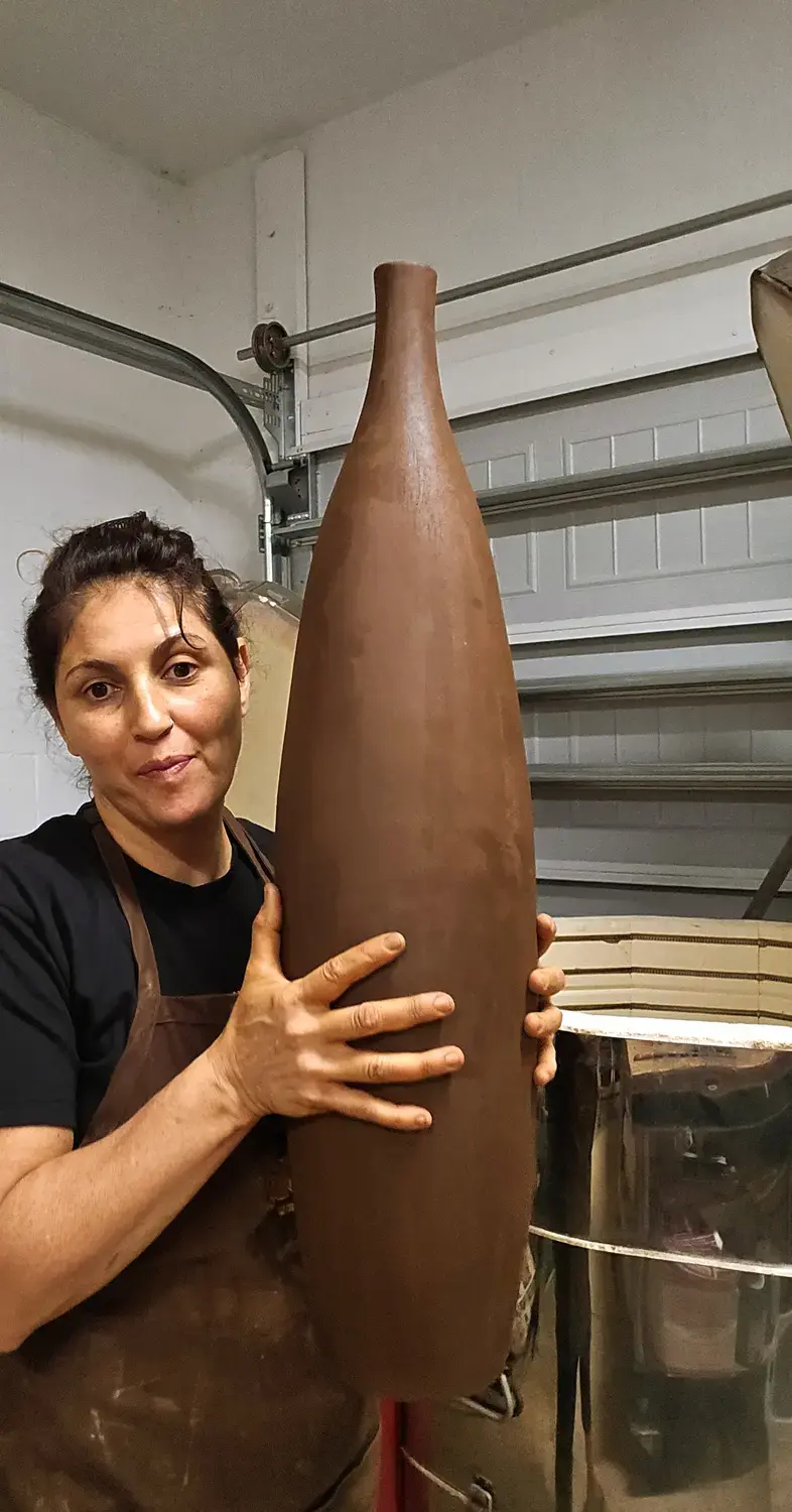 Maria holding a tall clay sculpture in the studio