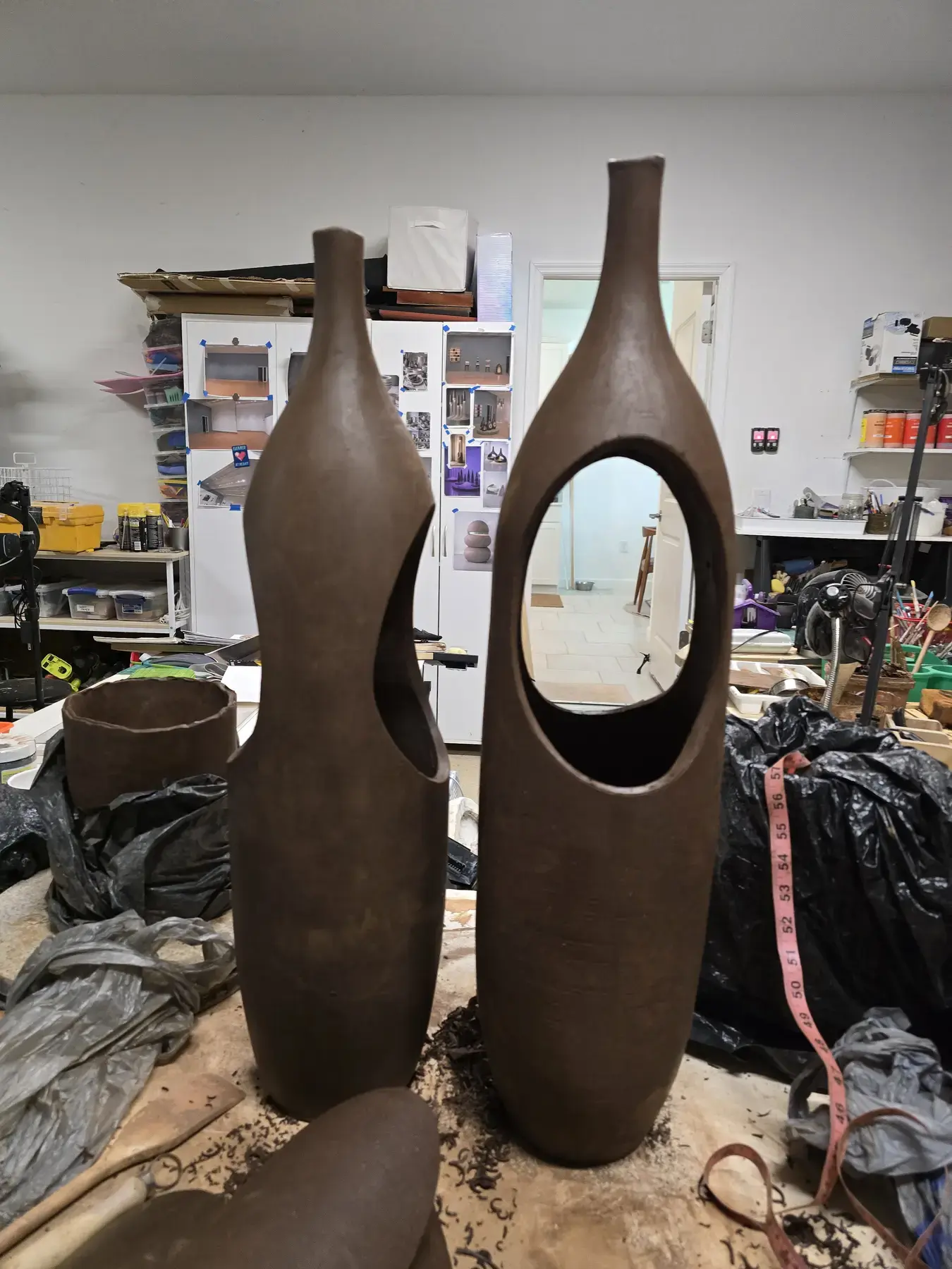 Two tall hand-built clay sculptures with open centers in the studio